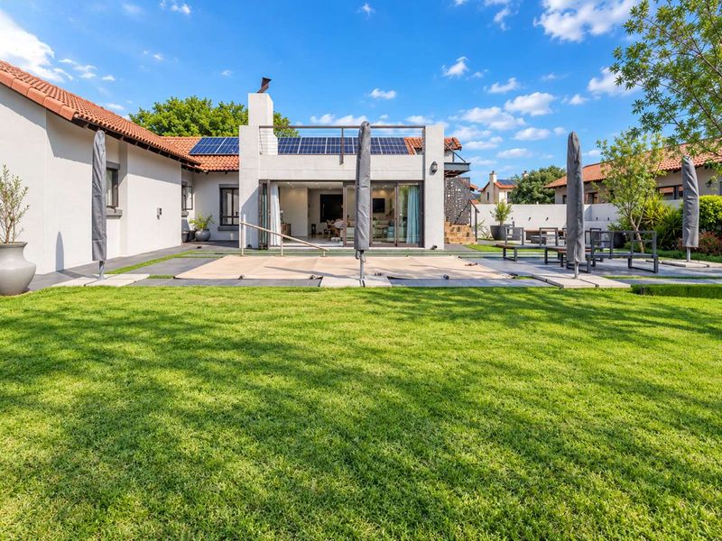 A well-maintained rear garden featuring a lawn, paved patio area, swimming pool with cover, and a modern home exterior with solar panels.