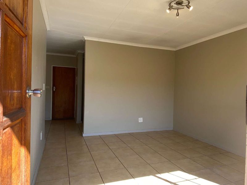 An empty living room featuring neutral wall tones, tiled flooring, and a simple ceiling light fixture, providing a blank canvas for interior design.