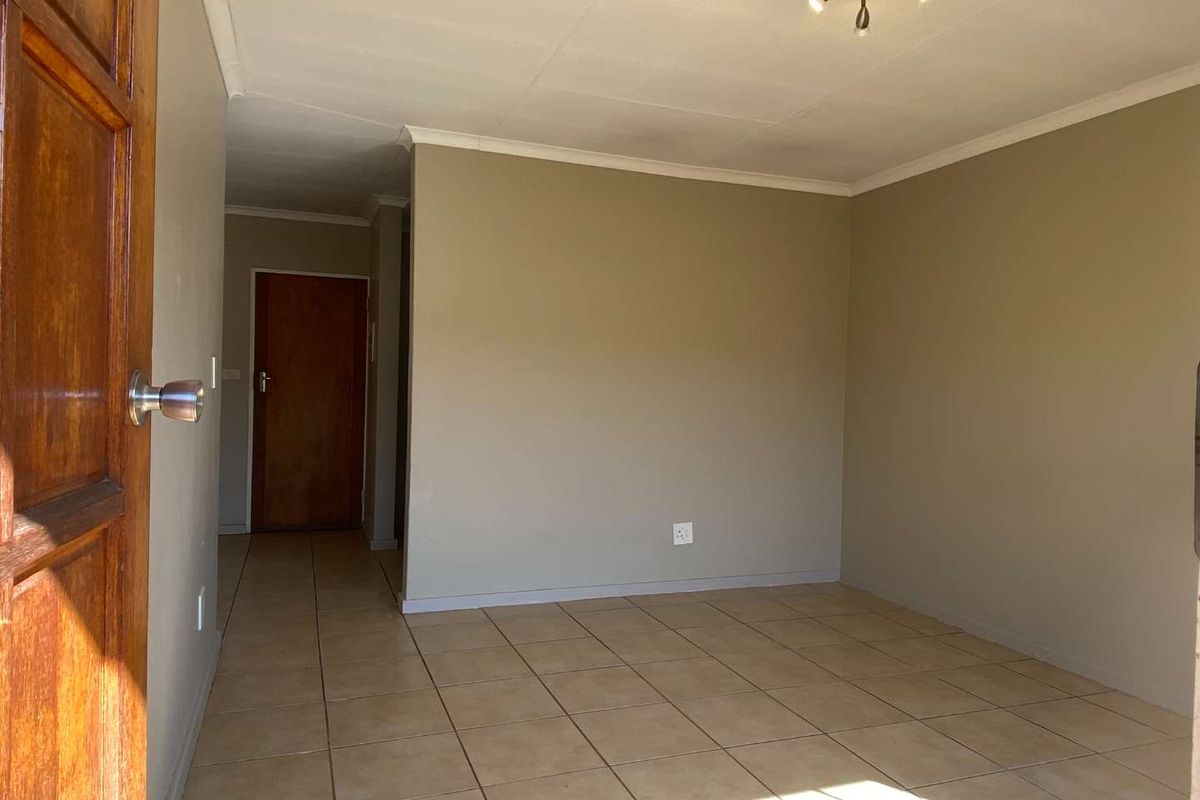 An empty living room featuring neutral wall tones, tiled flooring, and a simple ceiling light fixture, providing a blank canvas for interior design.