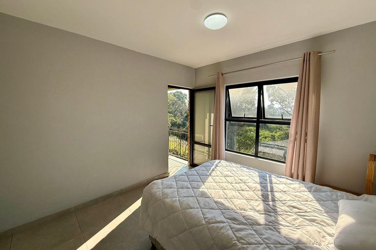 A bright bedroom featuring tiled flooring, a large window, and a door providing direct access to an outdoor balcony area.
