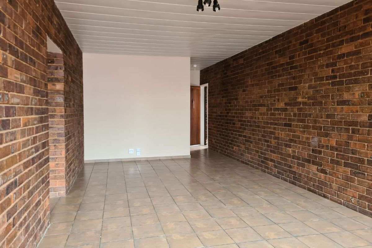 An empty living area featuring exposed brick walls, tiled flooring, and a panelled ceiling, offering a blank canvas for interior design.