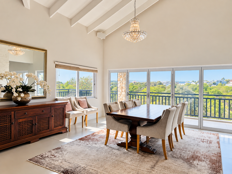 Elegant dining room featuring a high vaulted ceiling with exposed rafters, a crystal chandelier, and expansive glass doors opening to a scenic balcony.