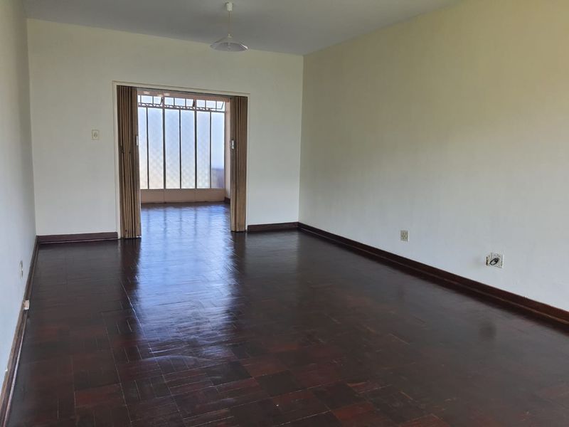 Spacious, empty living area featuring dark parquet flooring and a folding room divider leading to an adjacent sunroom or balcony space.