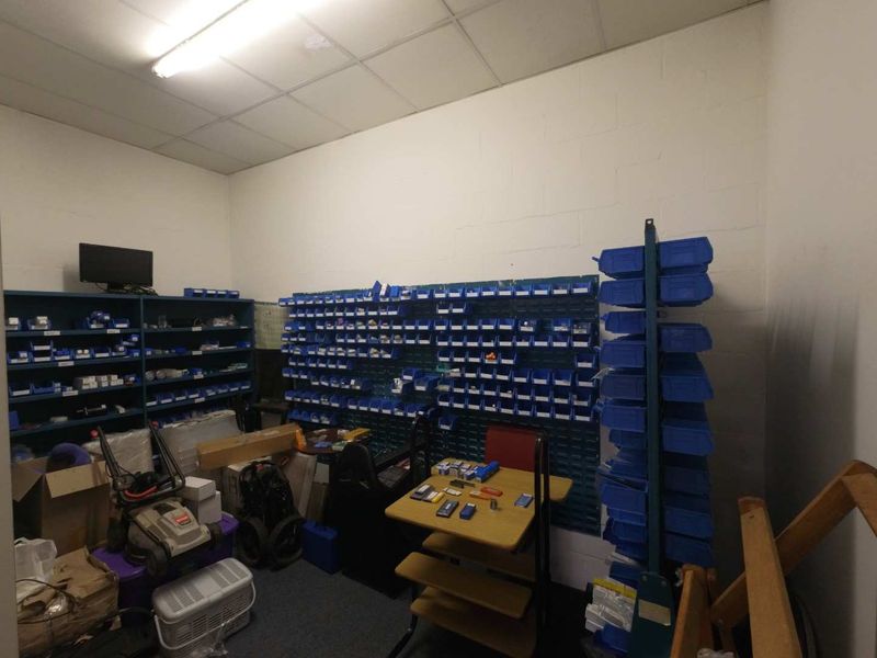 A functional industrial utility or storage room featuring wall-mounted shelving units, suspended ceiling, and painted masonry walls, suitable for inventory or equipment organization.