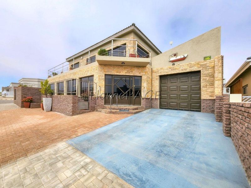 Front elevation of a multi-level house featuring stone cladding, a paved driveway, a sectional garage door, and an upper-level balcony with metal railings.