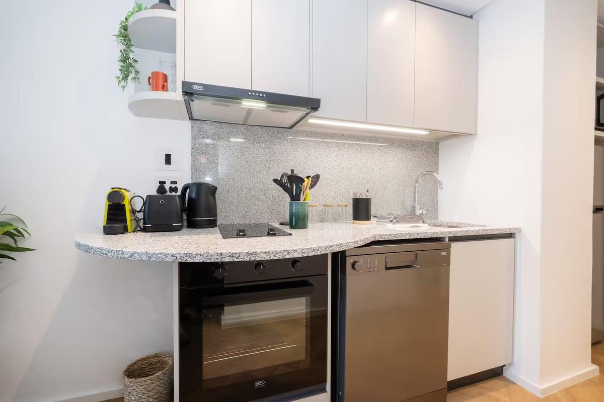 Modern compact kitchen featuring granite countertops, built-in oven, electric hob, extractor fan, and sleek cabinetry with integrated sink.