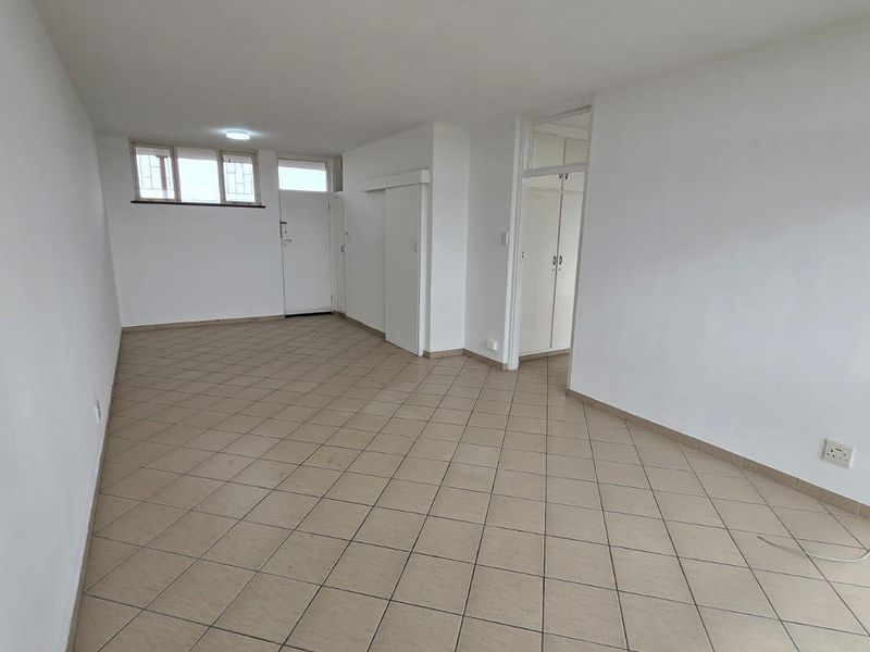 An empty, open-plan living area featuring neutral tiled flooring, built-in storage cupboards, and security bars on the windows.