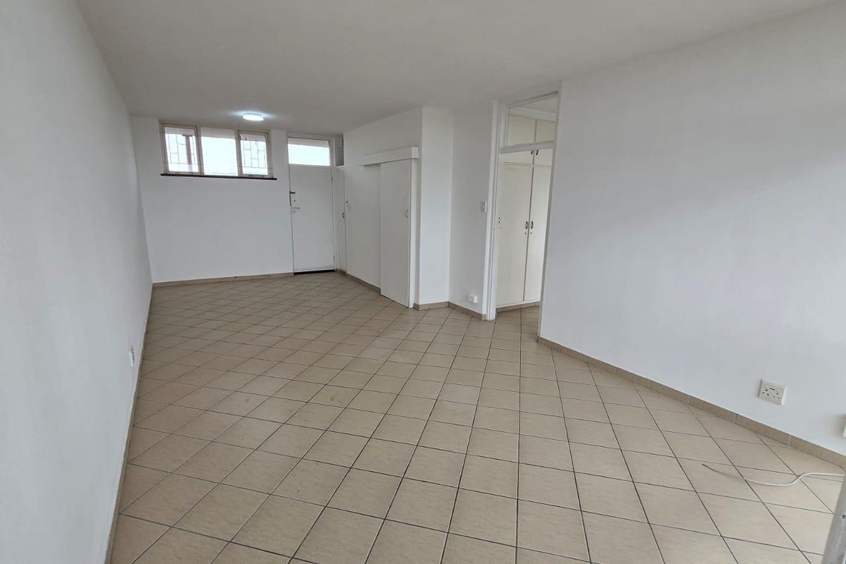 An empty, open-plan living area featuring neutral tiled flooring, built-in storage cupboards, and security bars on the windows.