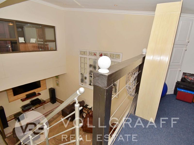 An elevated view from a landing area overlooking the living space below, featuring a staircase with a metal balustrade and built-in storage cabinetry.