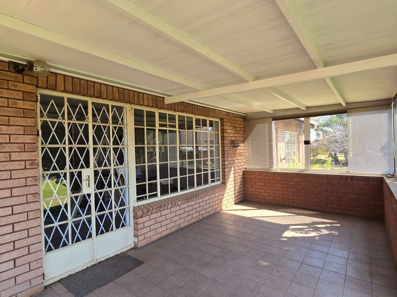 A covered patio area featuring tiled flooring, exposed brick walls, and secure metal gate access, providing a functional outdoor living space.