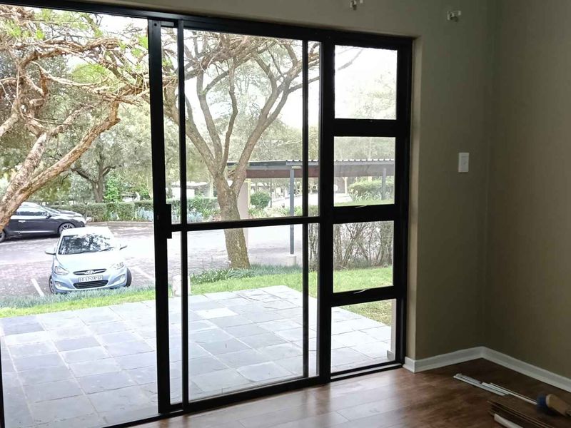 An empty living room featuring laminate flooring and a large black aluminium sliding door providing access to an outdoor patio area.