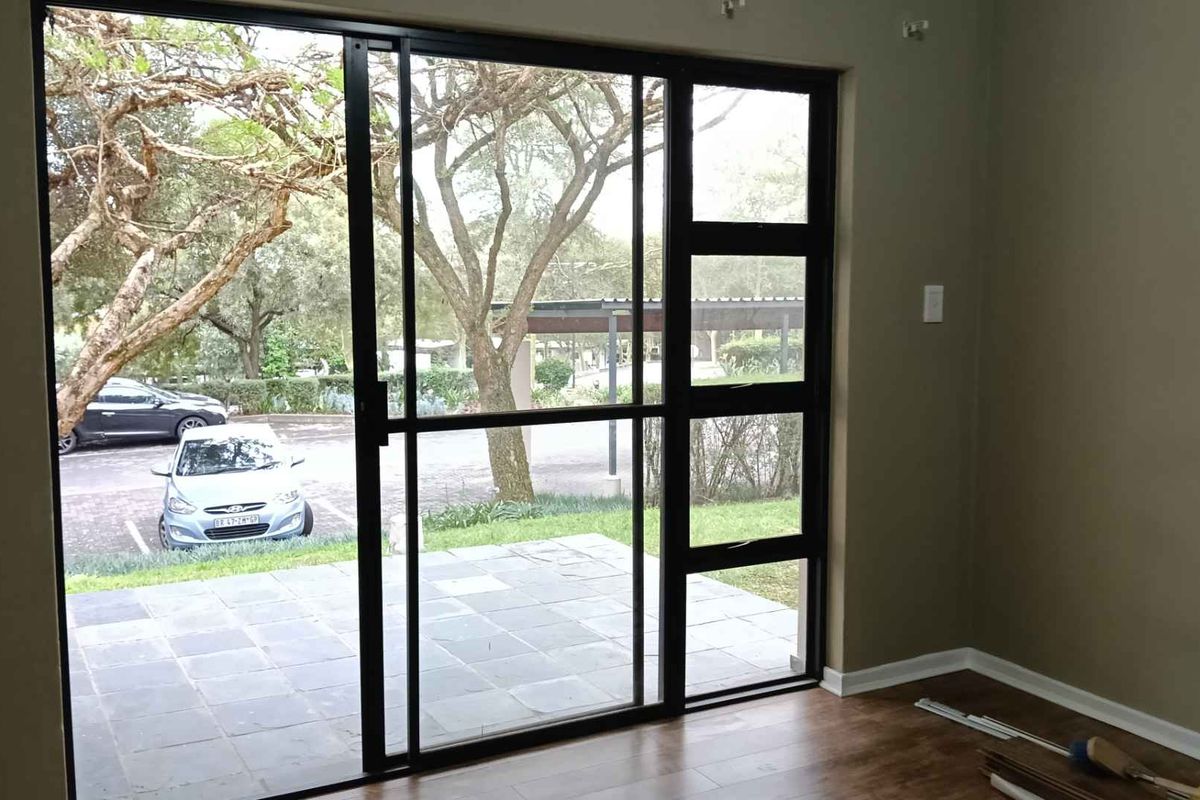 An empty living room featuring laminate flooring and a large black aluminium sliding door providing access to an outdoor patio area.