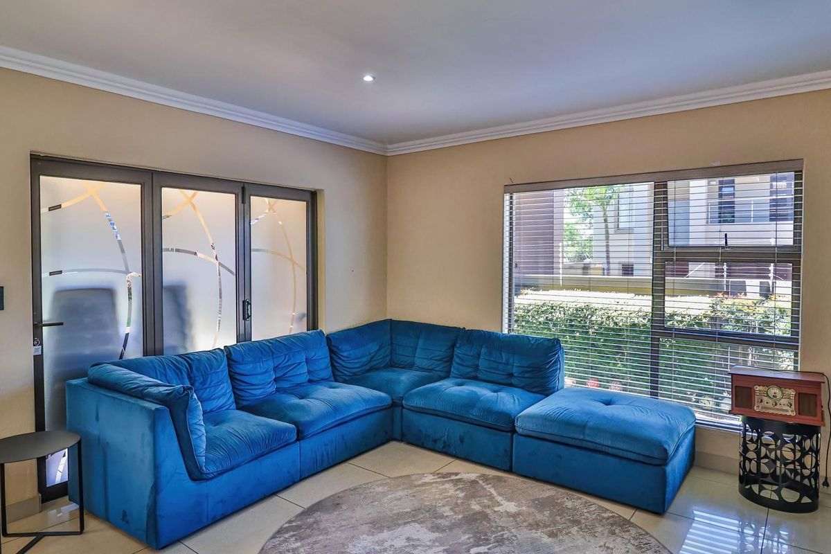 A bright living room featuring tiled flooring, aluminium window frames with venetian blinds, and modern sliding doors leading to the exterior.