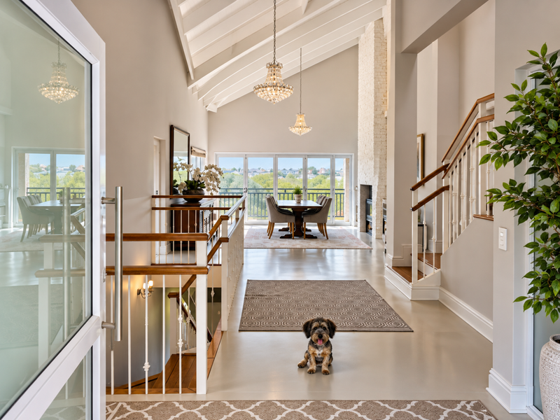 Spacious open-plan living and dining area featuring vaulted ceilings, exposed rafters, crystal chandeliers, and a prominent brick fireplace with views through sliding glass doors.