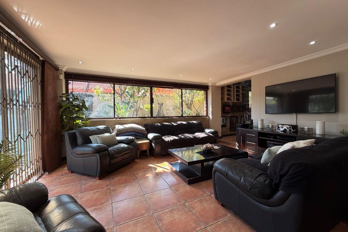Spacious living room featuring terracotta floor tiles, recessed downlighting, and large windows providing natural light and views of the garden.