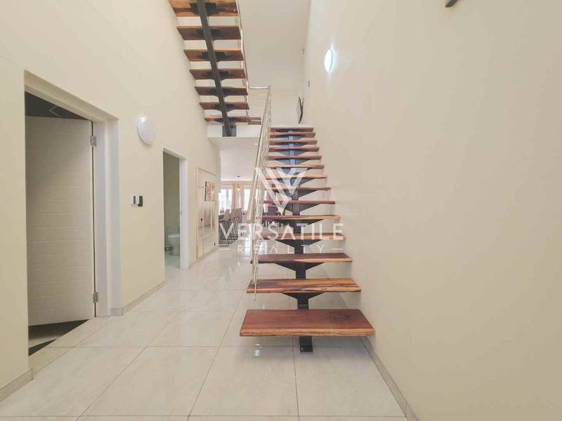 A bright, modern hallway featuring a striking floating staircase with timber treads and a sleek metal balustrade, finished with polished floor tiles.
