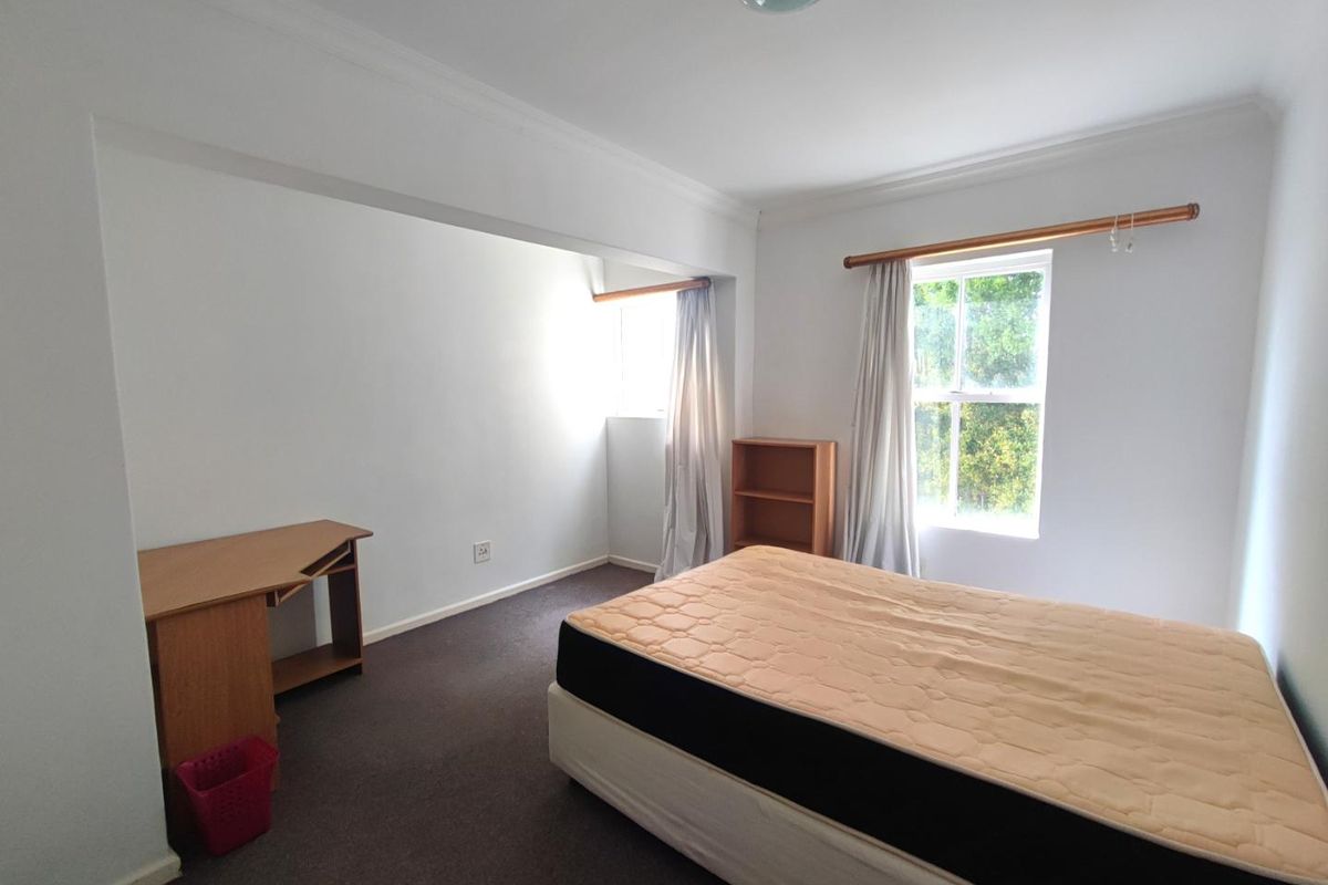 A spacious bedroom featuring neutral walls, carpeted flooring, and natural light from the window, offering a versatile layout for bedroom or home office use.
