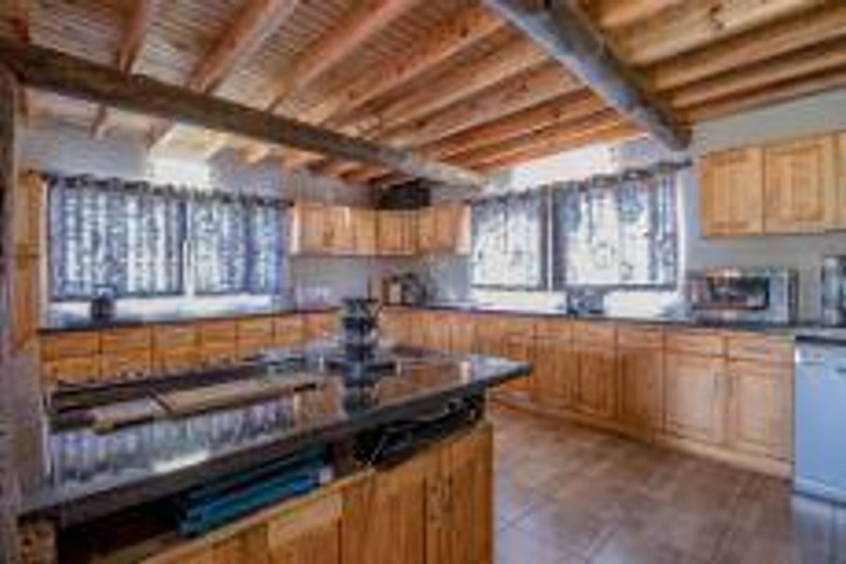 Rustic kitchen featuring extensive wooden cabinetry, dark granite countertops, a central island, and exposed timber ceiling beams.