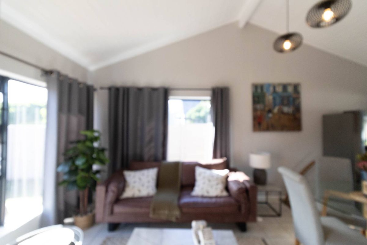 A bright living area featuring a vaulted ceiling, tiled flooring, and large windows that provide ample natural light.