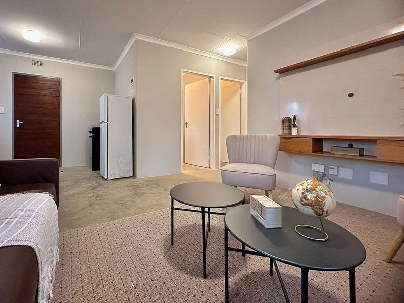 A living room featuring a mix of carpeted and concrete flooring, built-in wall shelving, and access to adjacent rooms.