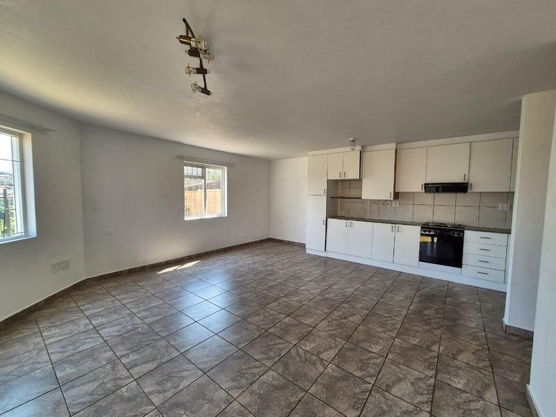 Spacious open-plan living area featuring tiled flooring and a functional kitchen with built-in cabinetry, oven, and hob.