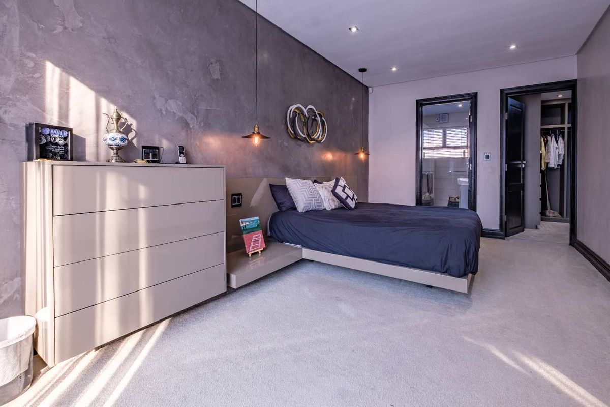 A modern bedroom featuring a textured feature wall, recessed lighting, carpeted floors, and convenient access to an en-suite bathroom and walk-in closet.