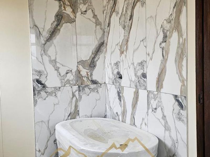 A modern bathroom featuring a new freestanding bathtub set against elegant marble-look wall tiles, currently in the final stages of completion.