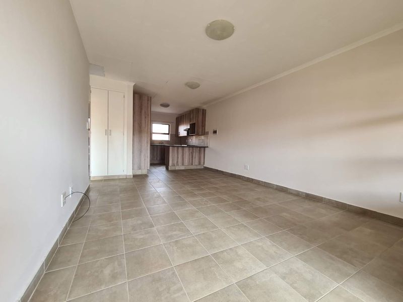 An open-plan living and kitchen area featuring neutral tiled flooring, built-in cabinetry, and a functional layout, presented in a clean, vacant condition.
