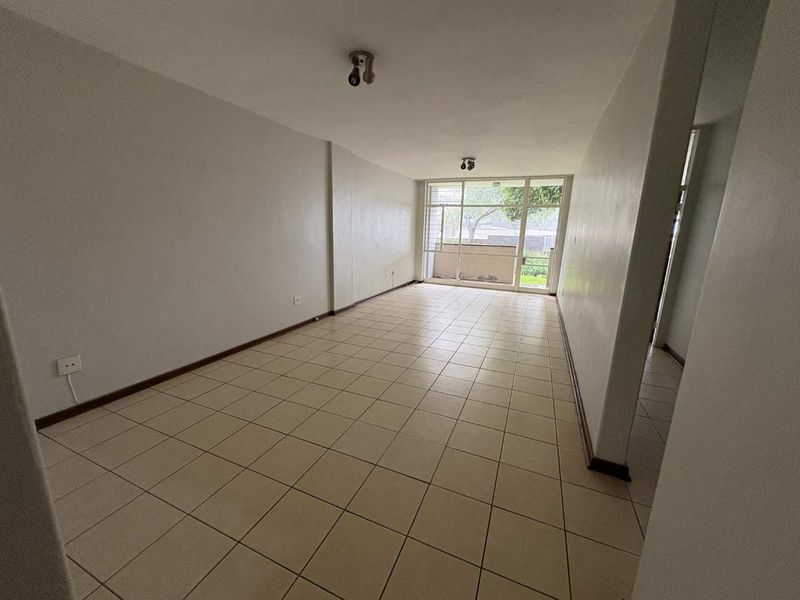 An empty, open-plan living area featuring neutral ceramic floor tiles and a large sliding glass door providing access to an outdoor space.