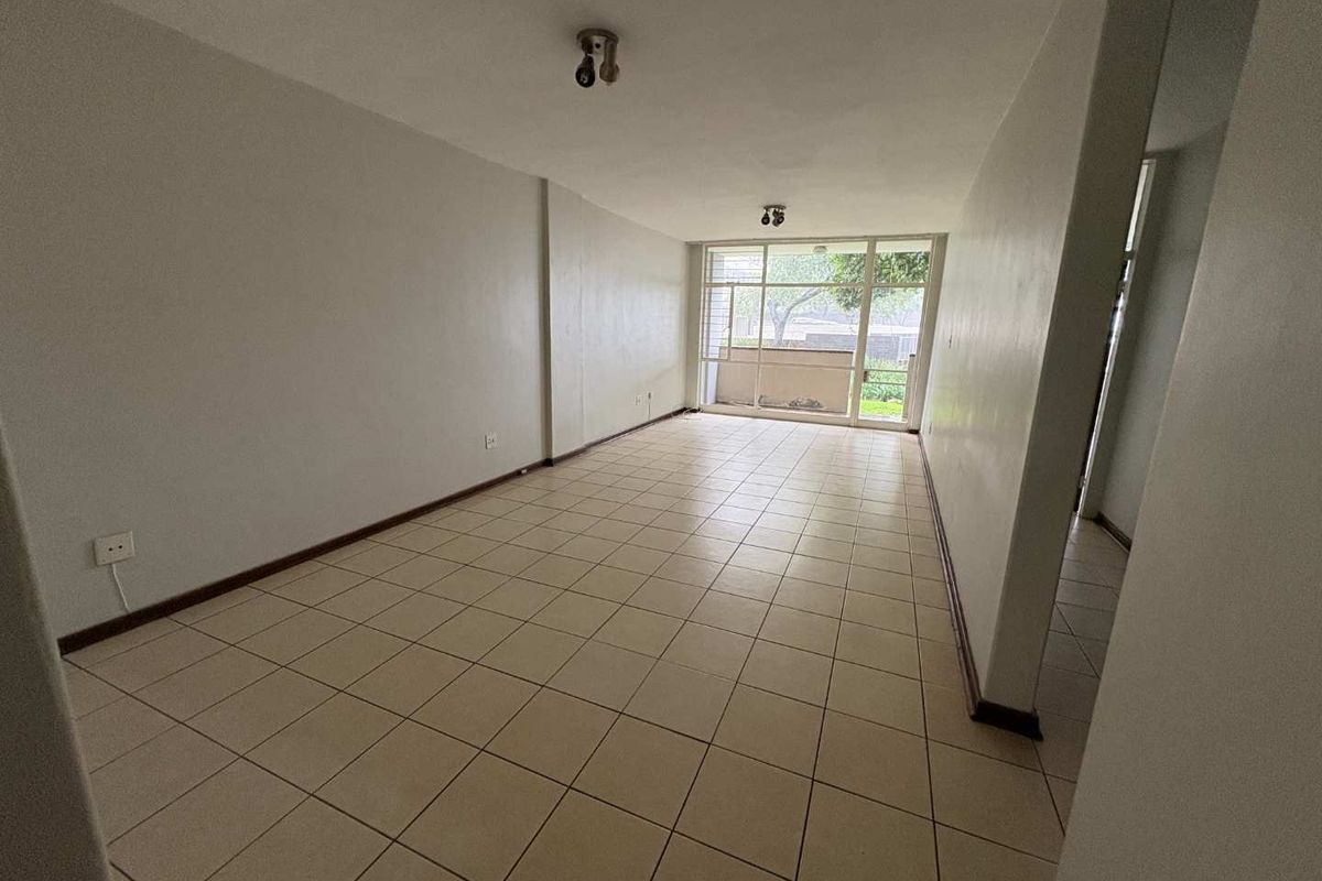 An empty, open-plan living area featuring neutral ceramic floor tiles and a large sliding glass door providing access to an outdoor space.