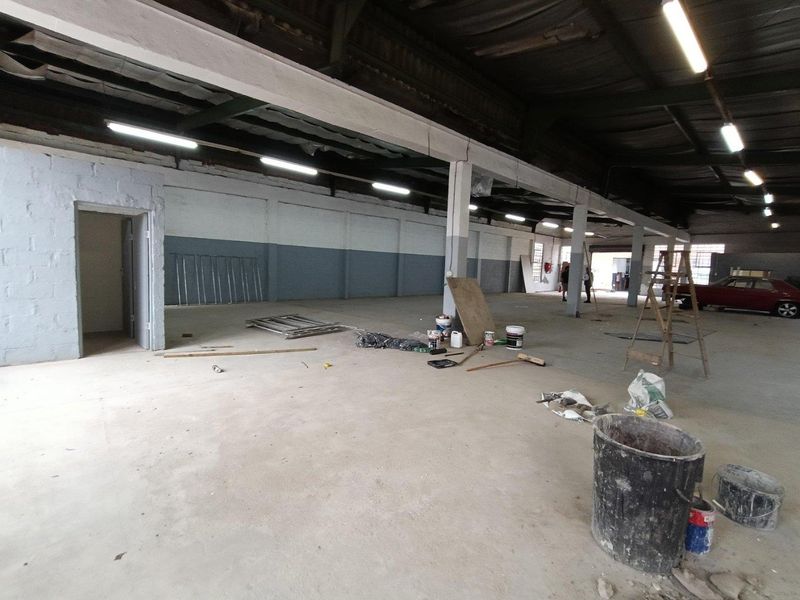 Spacious industrial utility area featuring exposed steel roof trusses, concrete flooring, and functional strip lighting, suitable for warehouse or workshop use.