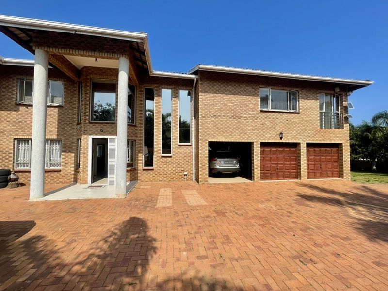 A well-maintained double-story face brick home featuring a spacious paved driveway, double garage, and a covered entrance porch with prominent concrete columns.