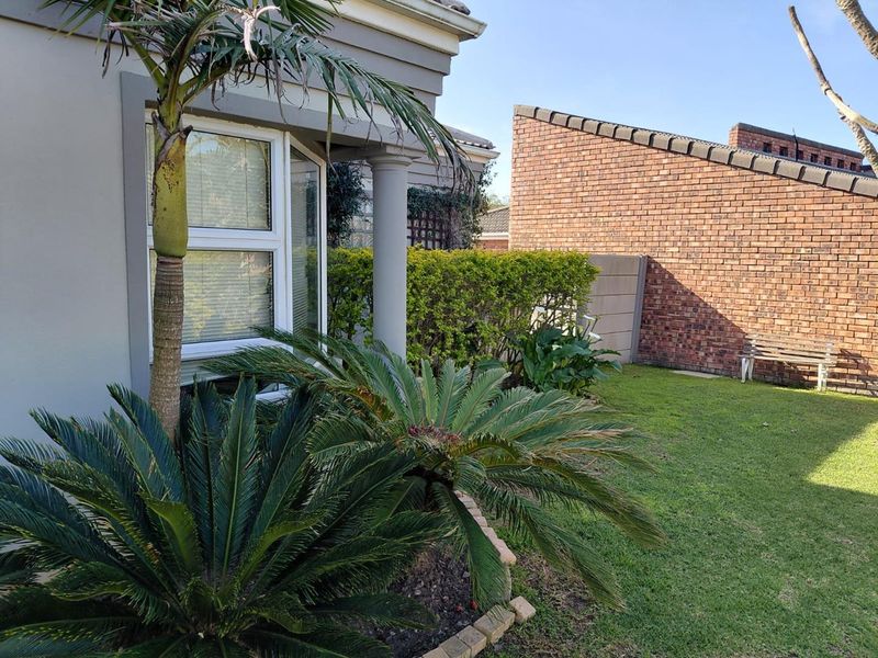 A well-maintained rear garden area featuring a bay window, brick boundary wall, and established landscaping.