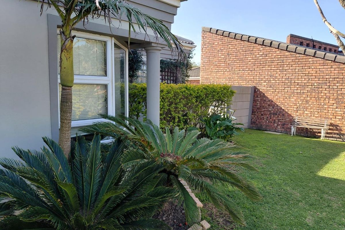 A well-maintained rear garden area featuring a bay window, brick boundary wall, and established landscaping.