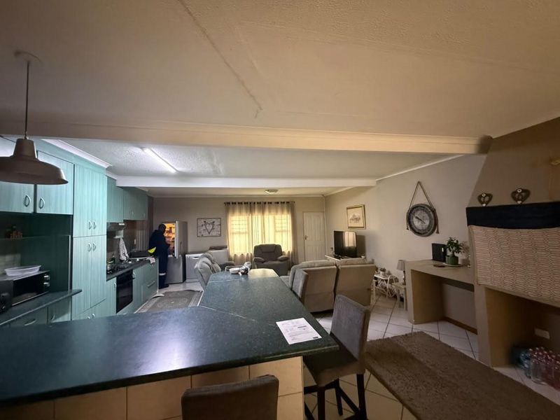 Open-plan living area featuring a kitchen with built-in cabinetry, a central island, and a built-in fireplace, finished with tiled flooring throughout.