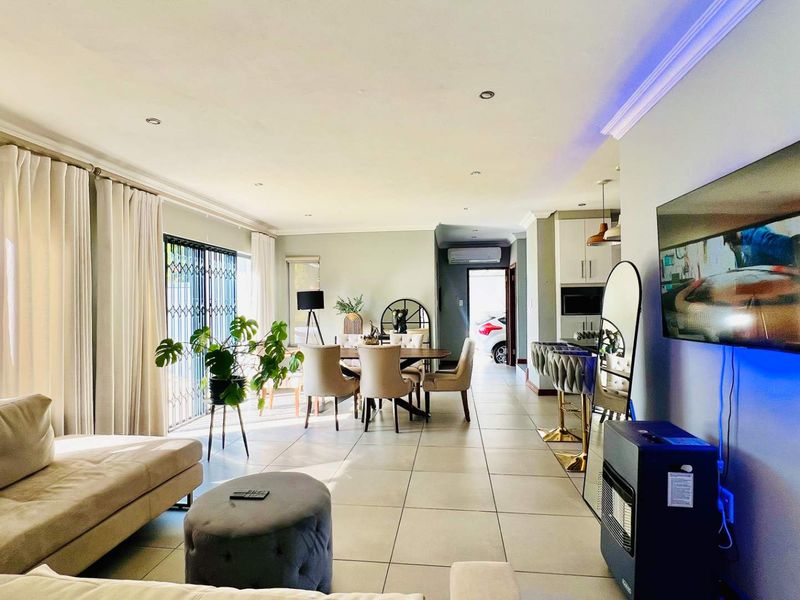 Spacious open-plan living and dining area featuring large format floor tiles, recessed lighting, and seamless flow to the outdoor patio through sliding glass doors.