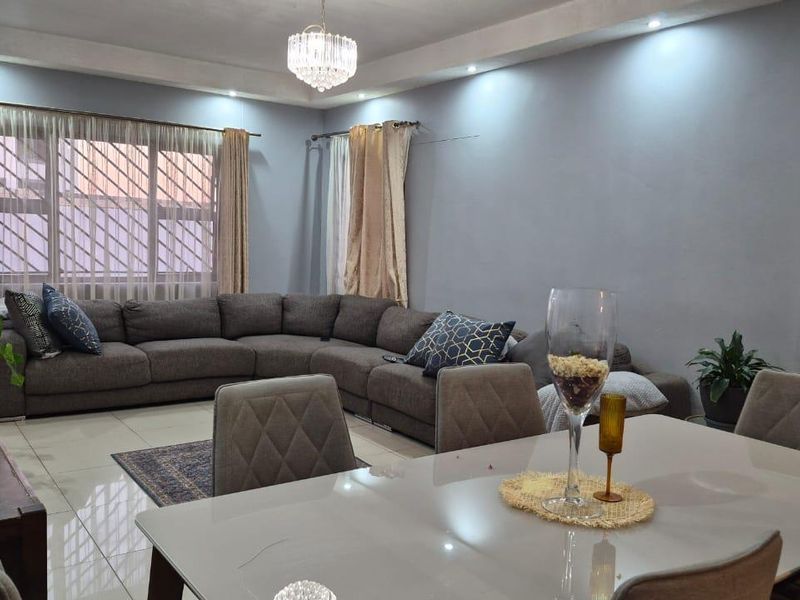 Spacious open-plan living and dining area featuring tiled flooring, recessed ceiling lighting, and a decorative crystal chandelier.