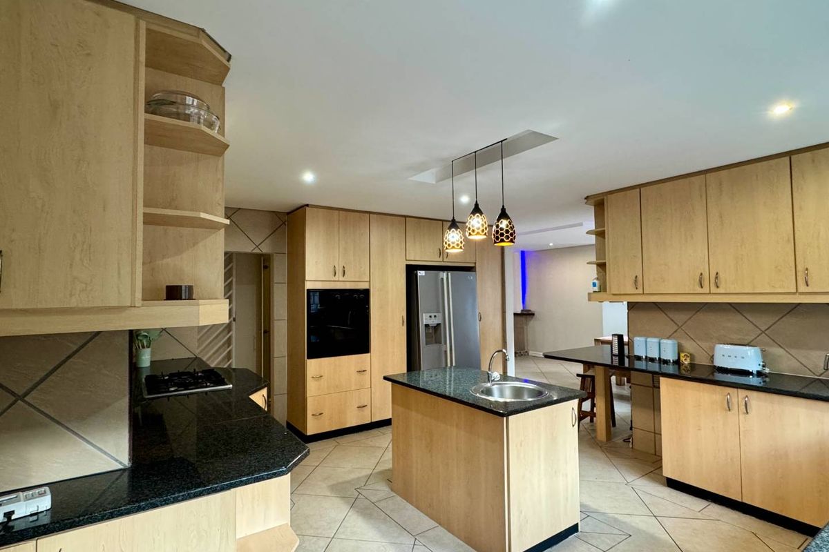 Spacious kitchen featuring light wood cabinetry, dark granite countertops, a central island with a prep sink, and integrated oven.