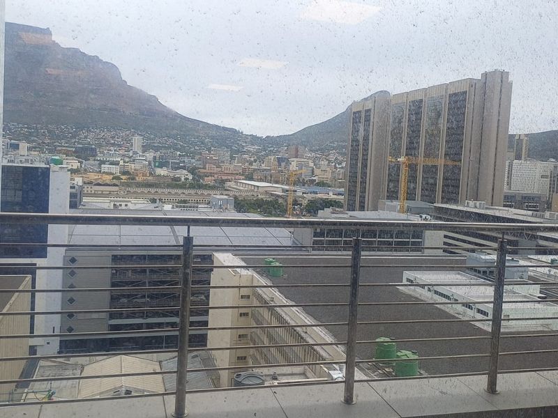 An elevated city and mountain view captured from a balcony with a stainless steel balustrade.