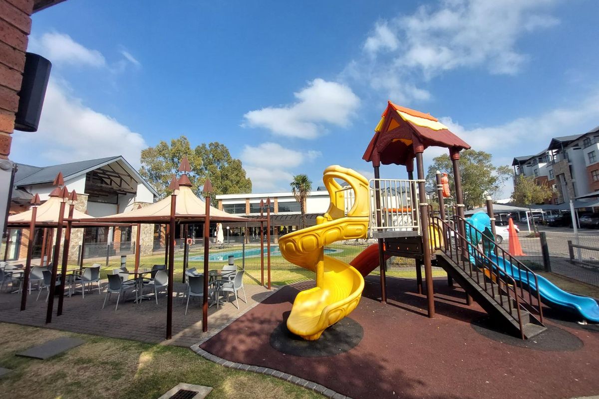Communal outdoor area featuring a children's playground, paved patio with gazebo, and swimming pool access within the apartment complex.