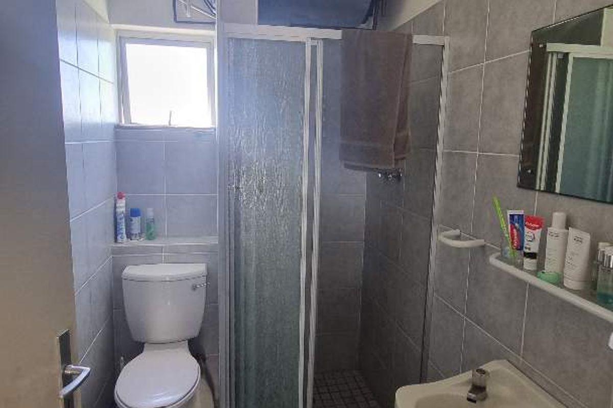 A functional bathroom featuring a shower enclosure, toilet, and wall-mounted basin, with an exposed water heater unit above the shower.