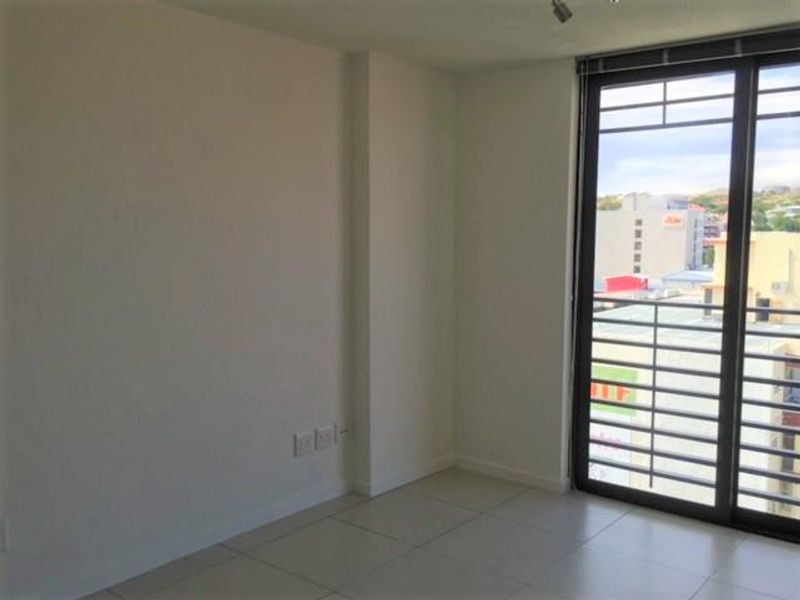 An empty living area featuring neutral tiled flooring and a large sliding glass door with security bars, offering an urban city view.