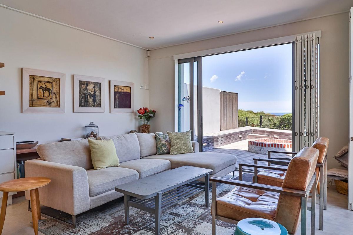 Bright living room featuring large sliding glass doors that open onto a wooden deck with an outdoor fire pit and ocean views.