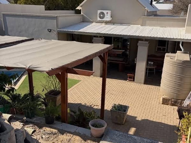 Rear exterior view featuring a paved courtyard, covered patio area, timber pergola, and a water storage tank set against the main house structure.