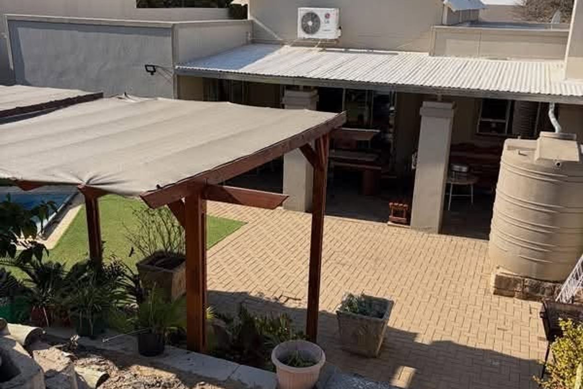 Rear exterior view featuring a paved courtyard, covered patio area, timber pergola, and a water storage tank set against the main house structure.