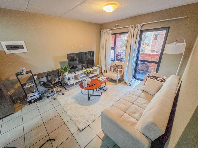A living room featuring tiled flooring, a large window, and a sliding glass door providing access to an outdoor area.