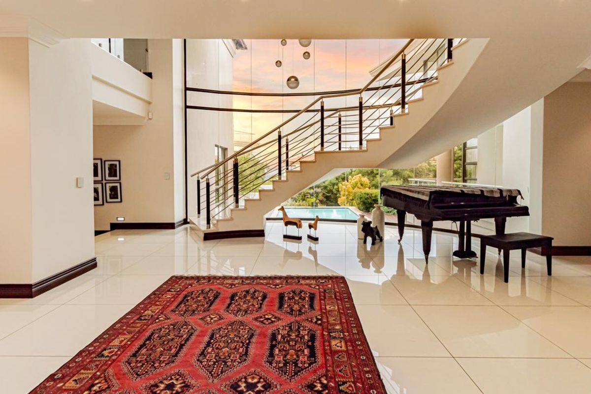 Spacious living area featuring a grand curved staircase, floor-to-ceiling windows with pool views, polished tile flooring, and a sophisticated stone feature wall.