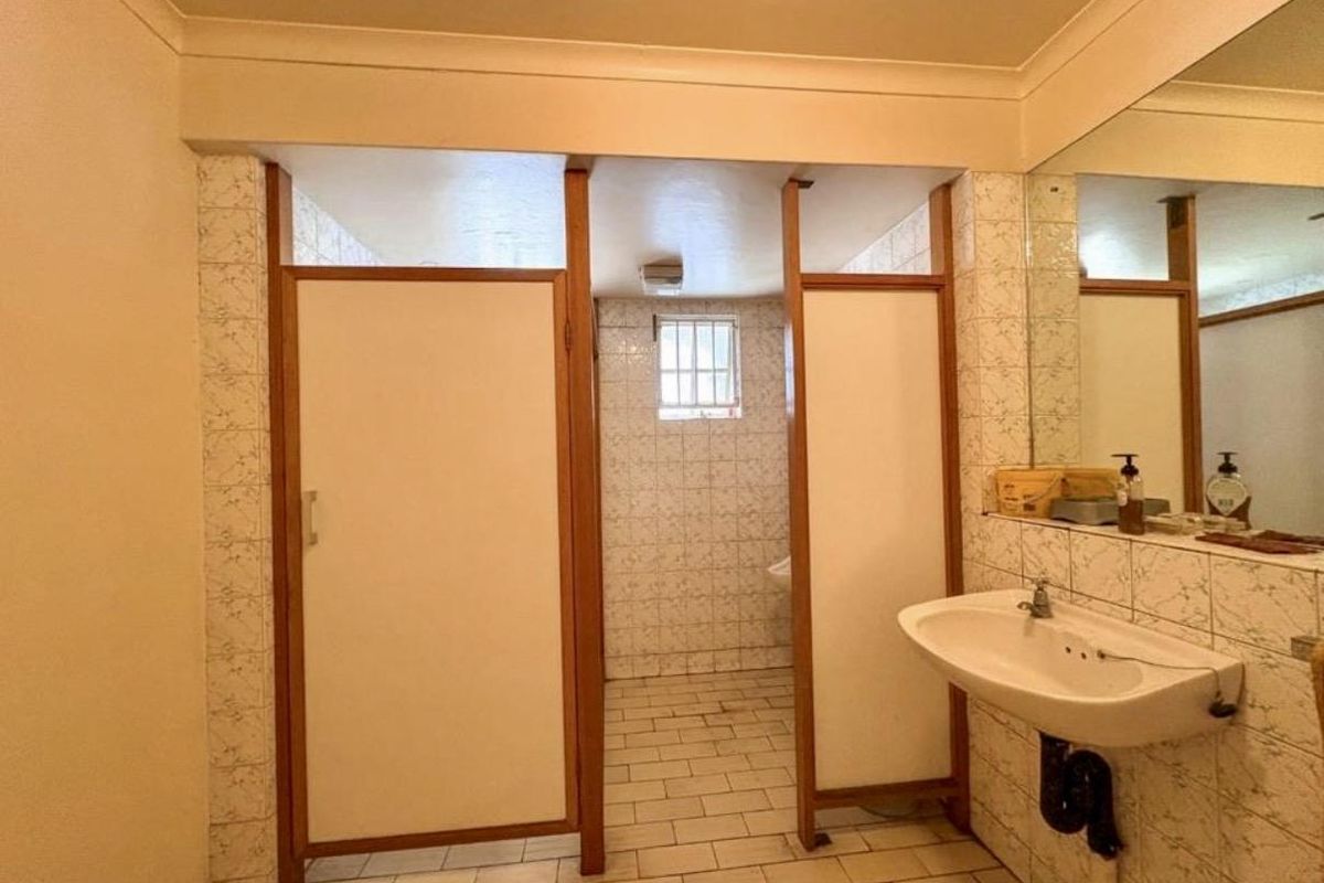 A functional industrial-style bathroom featuring multiple partitioned stalls, a wall-mounted basin, and tiled surfaces throughout.
