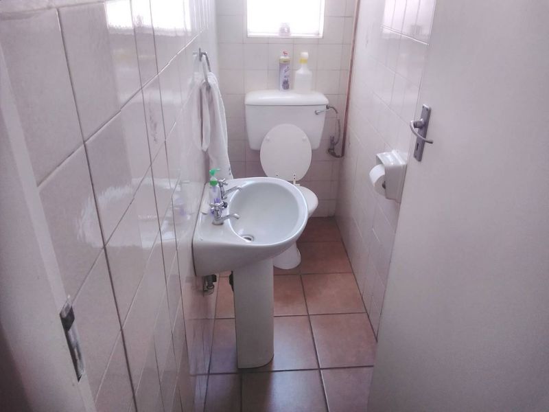 A compact guest bathroom featuring a pedestal basin and toilet with full-height ceramic wall tiling and tiled flooring.
