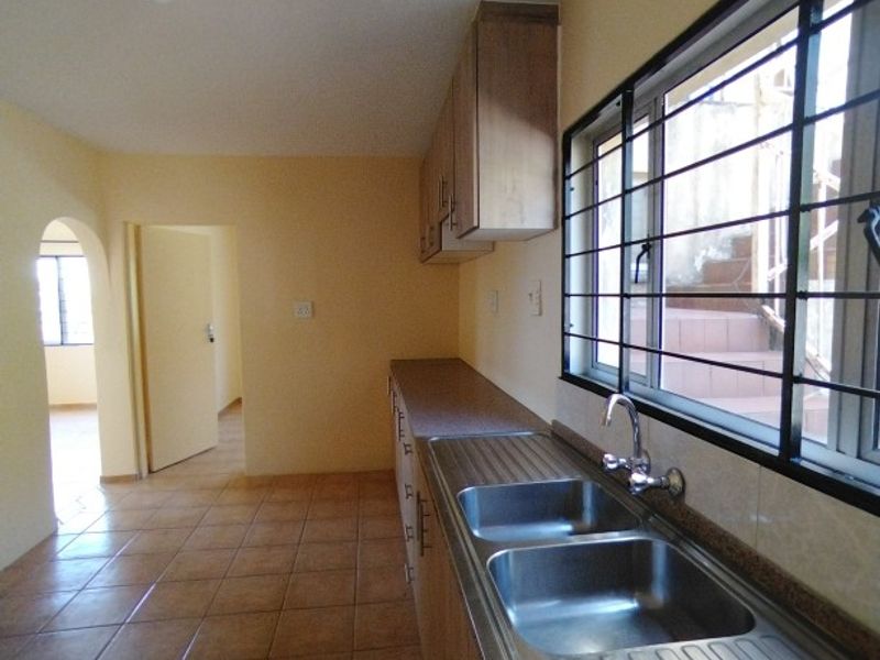 A functional kitchen featuring tiled flooring, built-in cabinetry, and a double stainless steel sink with a view through a window with security bars.